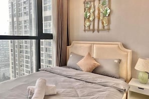 A hotel room with a large bed, a nightstand, a decorative wall piece, and a view of tall buildings.
