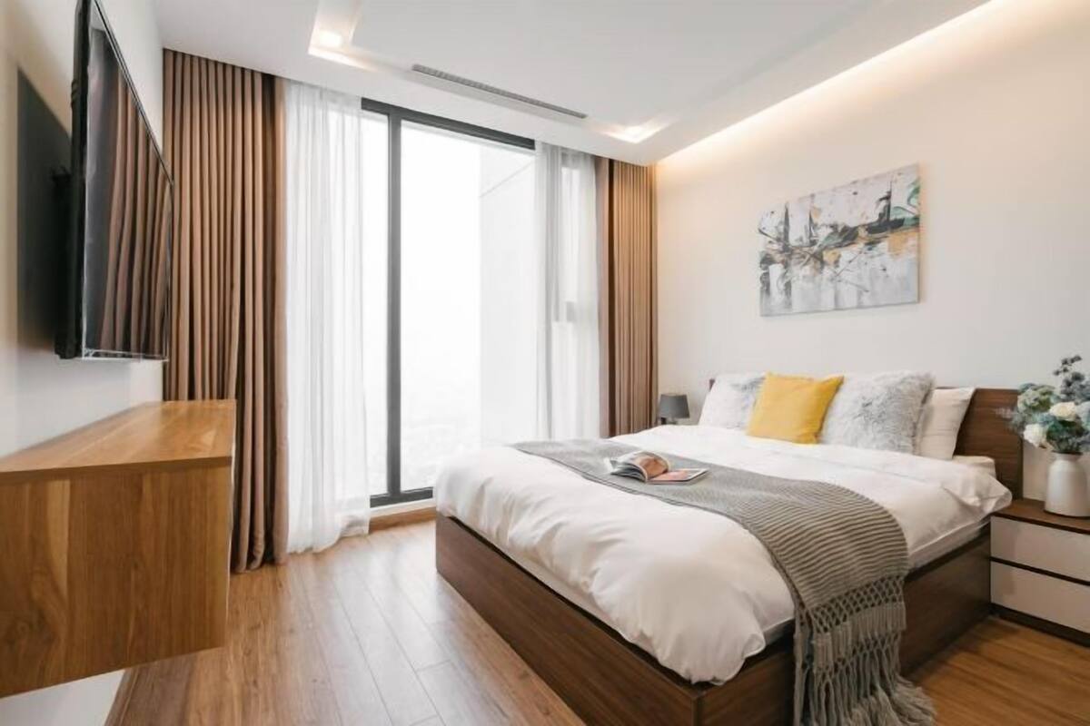 Une chambre moderne avec un lit, une table de chevet, une télévision et une grande fenêtre.