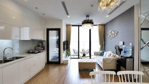 A modern kitchen with white cabinets, a dining area with a table and chairs, and a living room with a sofa and a chandelier.
