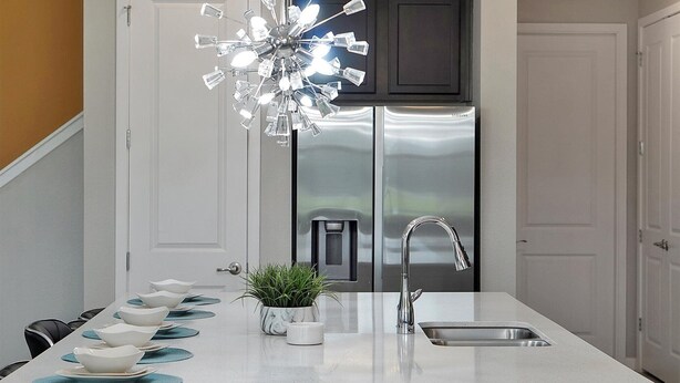 A modern kitchen with a central island, stainless steel appliances, and a unique crystal chandelier.