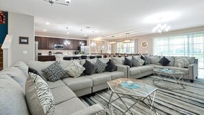 A spacious living room with a sectional sofa, a glass coffee table, and a kitchen in the background.
