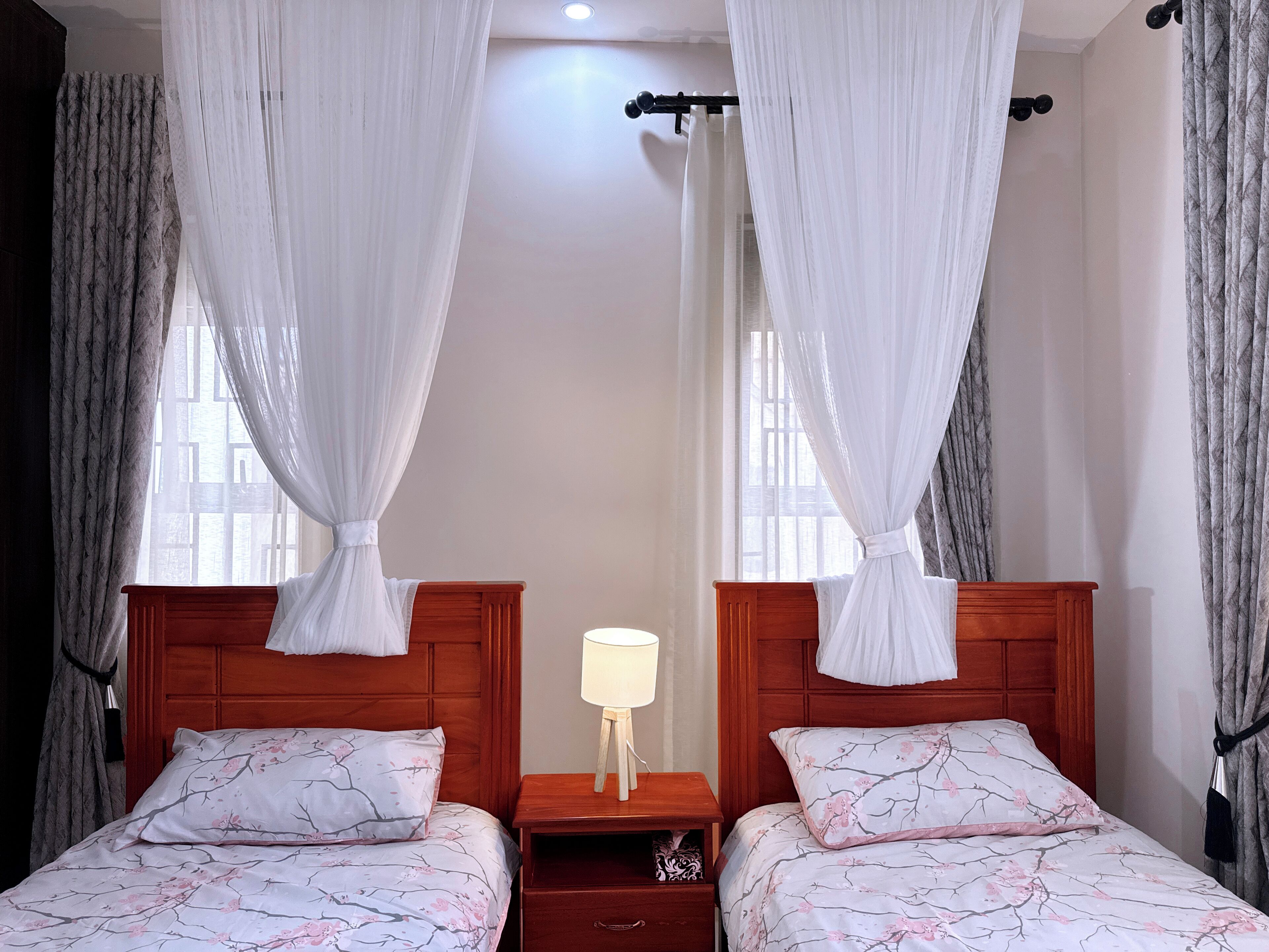 Habitación de hotel con dos camas, cada una con dosel, mesita de noche con lámpara y cortinas en las ventanas.