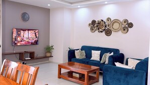 Uma sala de estar moderna com um sofá azul, mesa de centro de madeira e uma TV fixada na parede.