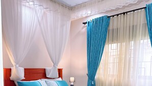 Quarto com cama de madeira, cortinas brancas e colcha azul.