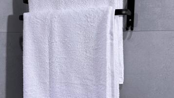 Una toalla blanca colgada en un perchero negro frente a una pared de azulejos.