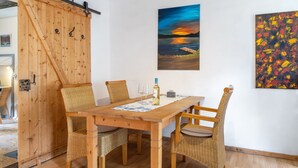 A dining area with a wooden table and wicker chairs, a painting of a sunset, and a rustic wooden door. - "Fuchsrevier" Apartment for Installers and Vacationers (Erkerode)