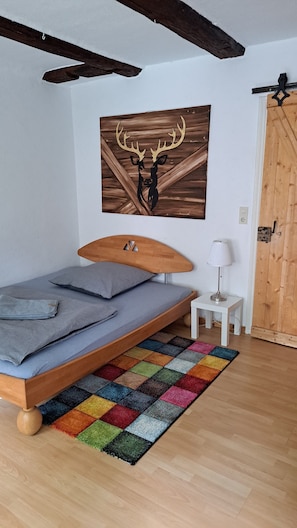 Ein Schlafzimmer mit einem Bett, einem farbenfrohen Teppich, einem Holz-Kopfteil, einem an der Wand befestigten Bild eines Hirschkopfes, einer Nachttischlampe und einer Holztür.
