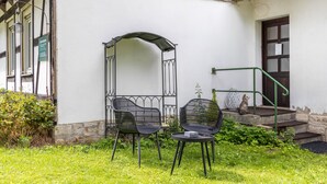 An outdoor seating area with two chairs and a table, a metal arch structure, and a staircase leading to a door.
