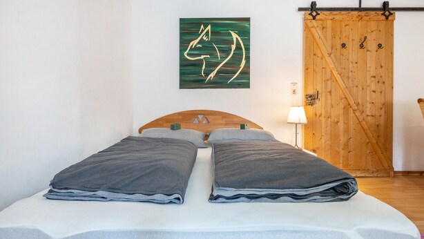 A bed with gray linens, a wooden headboard, and a green abstract painting on the wall.