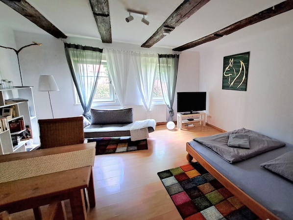 Ein Zimmer mit einem Bett, einem Fernseher, einem Bücherregal und einem Fenster mit Vorhängen.