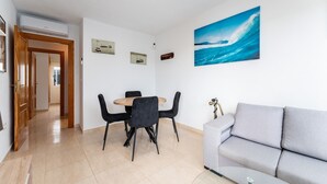 Un salon moderne avec un canapé gris, une table à manger avec des chaises noires, un tableau représentant une vague et un ventilateur de plafond.