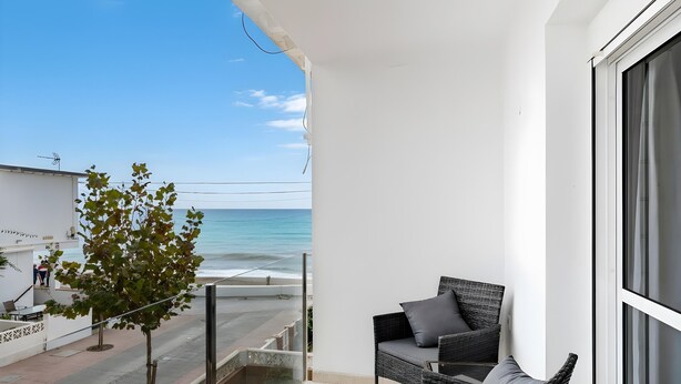 Un balcon avec un fauteuil en osier, un petit arbre et une vue sur l’océan.
