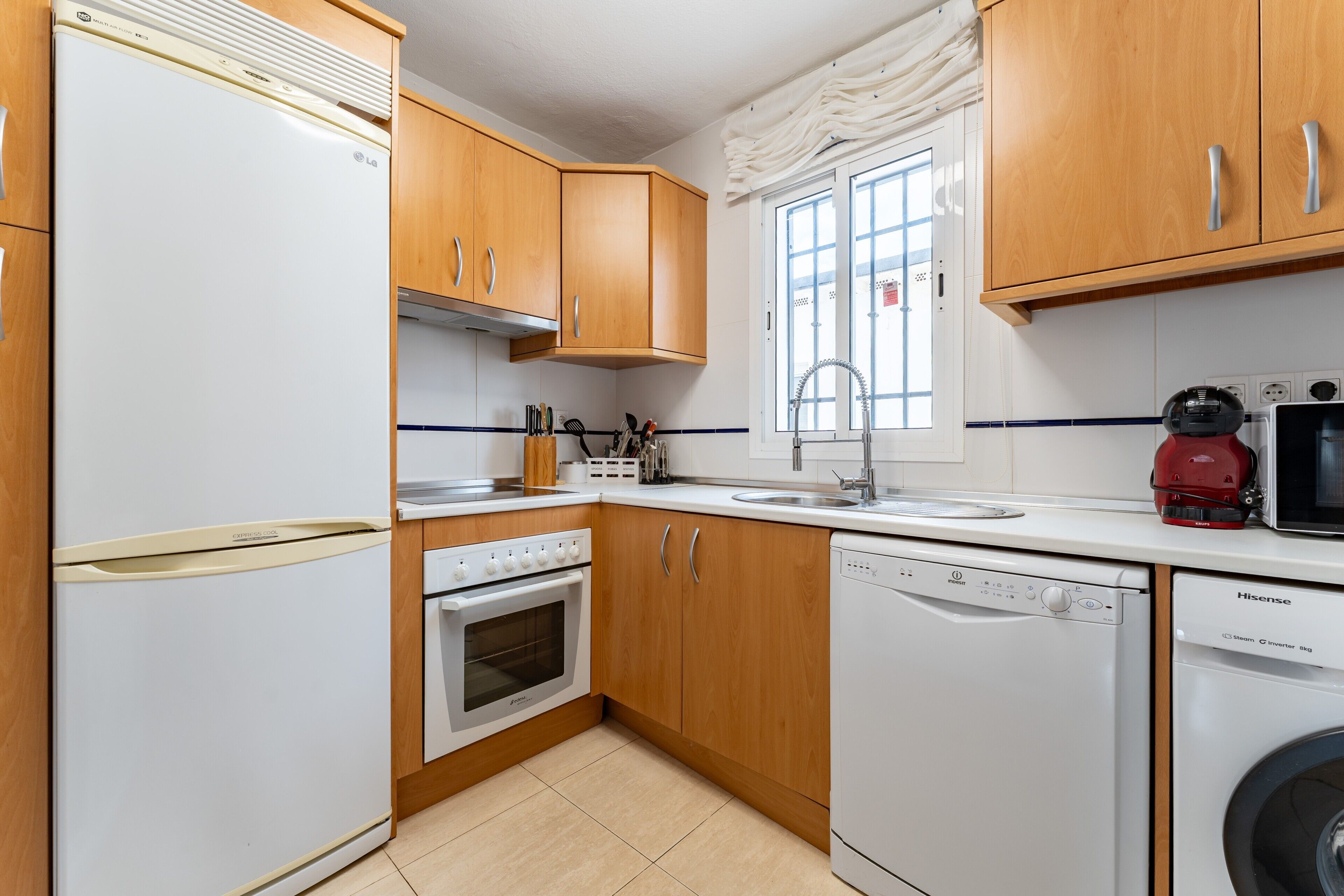 Une cuisine avec des meubles en bois, un réfrigérateur blanc, une cuisinière, un lave-vaisselle et une machine à café rouge.