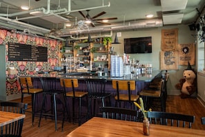 Un espace bar avec un tableau affichant le menu, des tabourets et une statue d’ours décorative.