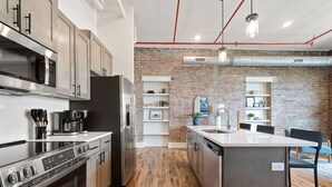 Una cocina moderna con electrodomésticos de acero inoxidable, piso de madera y pared de ladrillo.