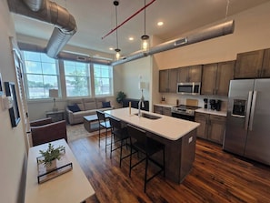 A modern kitchen with stainless steel appliances, a central island with bar stools, and a dining area with a sofa and chairs.