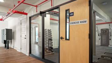 Una sala d'exercici amb una porta de fusta que porta la inscripció 'EXERCISE ROOM', una porta de vidre que dona a una paret amb miralls i un suport de peses amb bales.