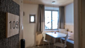 Una habitación con puerta de madera que tiene la etiqueta '105', un comedor con mesa y sillas, y una ventana con cortinas.