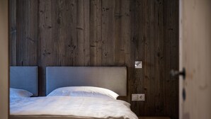 Un dormitorio con cabecera de madera, cama con ropa de cama blanca y mesita de noche con lámpara.