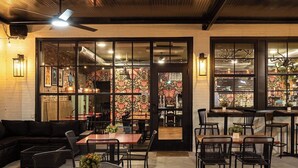 Un restaurant doté d’une terrasse, d’un mur en briques et d’une grande fenêtre ornée de motifs floraux.