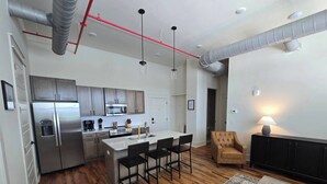 Una cocina moderna con electrodomésticos de acero inoxidable, una isla central con taburetes de bar, un sofá de cuero marrón y una alfombra estampada.