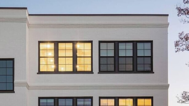 Un edificio de dos pisos con amplios ventanales, un patio cubierto con mesas al aire libre y un escaparate visible.