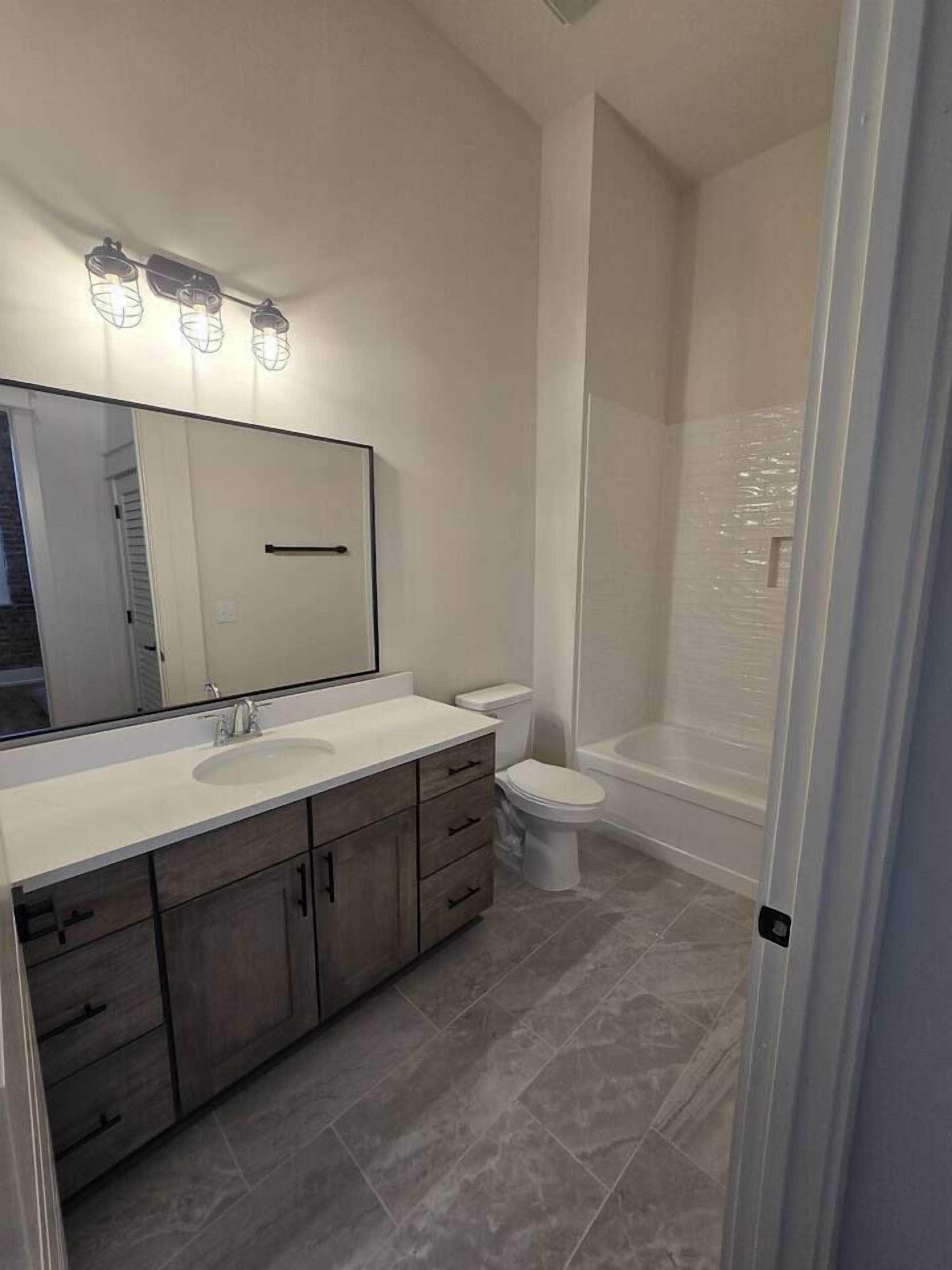 A bathroom with a large mirror, a sink, a toilet, and a shower area.