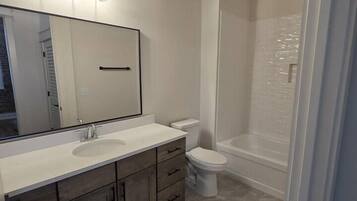 A bathroom with a large mirror, a sink, a toilet, and a shower area.