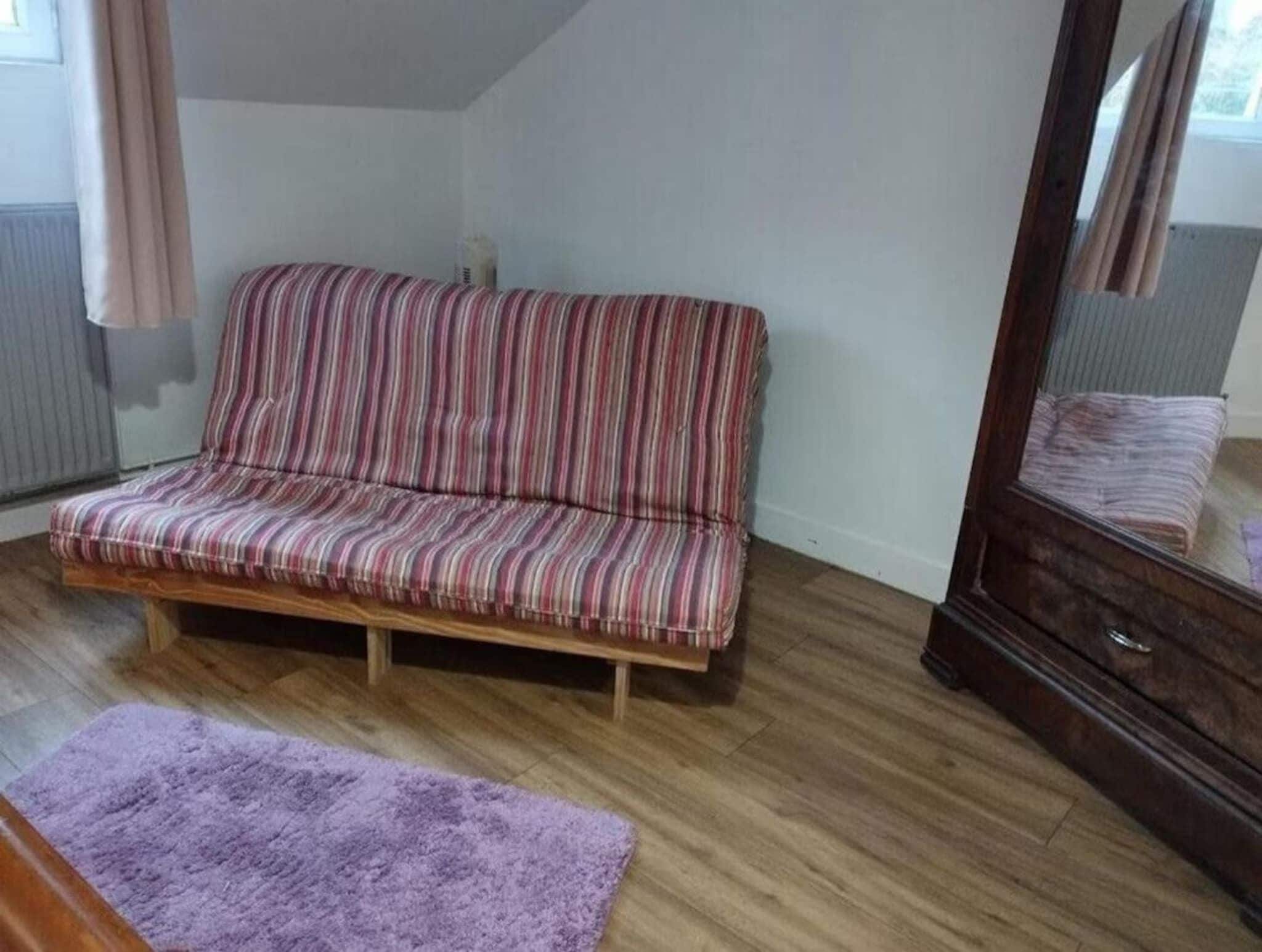 A room with a striped sofa, a wooden floor, a purple rug, and a mirror.