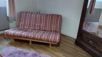 A room with a striped sofa, a wooden floor, a purple rug, and a mirror.