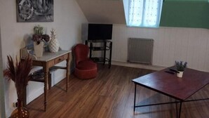 Ein Loft-Zimmer mit schrägem Dach, Holzboden, einem roten Sessel, einem Tisch, einem Fernseher und einem Fenster mit Blick.