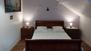 Ein Schlafzimmer mit schrägen Wänden, einem Bett mit zwei Kissen, zwei Nachttischlampen, einem kleinen Tisch und einem Gemälde an der Wand.