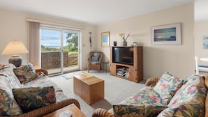 A living room with a sofa, a coffee table, a TV stand, and a lamp. - The Sound of Family: Shared Pier | Community Pools and More! (Nags Head)