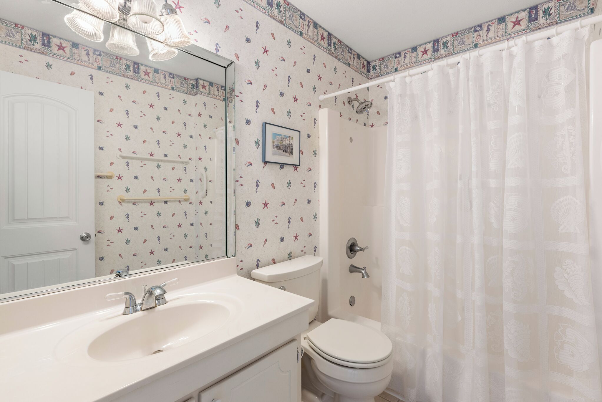 Un baño con lavamanos, espejo y retrete blancos. Las paredes tienen un diseño decorativo con estrellas y criaturas marinas.