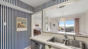 A modern kitchen with a double sink, stainless steel appliances, and a large mirror above the counter. - The Sound of Family: Shared Pier | Community Pools and More! (Nags Head)