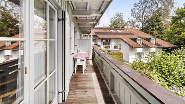 A narrow balcony with a wooden floor, white railings, and a view of neighboring houses.