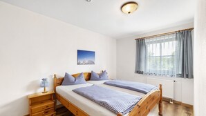 A double bed with a wooden frame, a bedside table with a lamp, a window with curtains, and a picture on the wall.