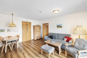 A living room with a wooden dining table, chairs, a sofa, a coffee table, and a lamp. - Apartment 'Fewo Brünnstein - No. 44 Pool, Sauna' with Mountain View, Shared Garden & Wi-Fi (Oberaudorf)