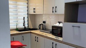 Une cuisine moderne avec des meubles blancs, un tabouret rouge, une bouilloire et une machine à café.