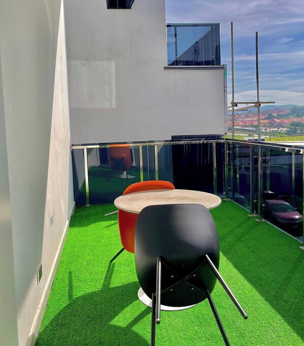 A modern outdoor seating area with a glass balustrade, a red chair, and a black chair on artificial green turf. - Akanchawa Homes  (Abuja)