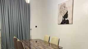 Un coin repas avec un sol carrelé en marbre, une table à manger en bois et quatre chaises, ainsi qu’un tableau accroché au mur.