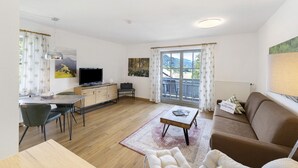 A living room with a sofa, a coffee table, a TV, and a dining area with chairs and a table.