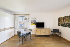 A modern kitchen with a dining area, wooden cabinets, a TV, and artwork on the walls.