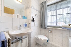 Casa de banho com lavatório branco, sanita e janela com cortinas.