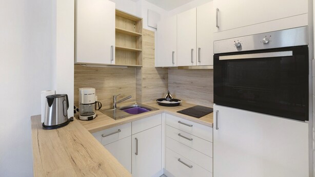 A modern kitchen with white cabinets, a built-in oven, a coffee maker, and a kettle.