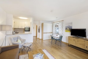 A modern living room with a sofa, a coffee table, a TV, and a dining area with chairs and a table.