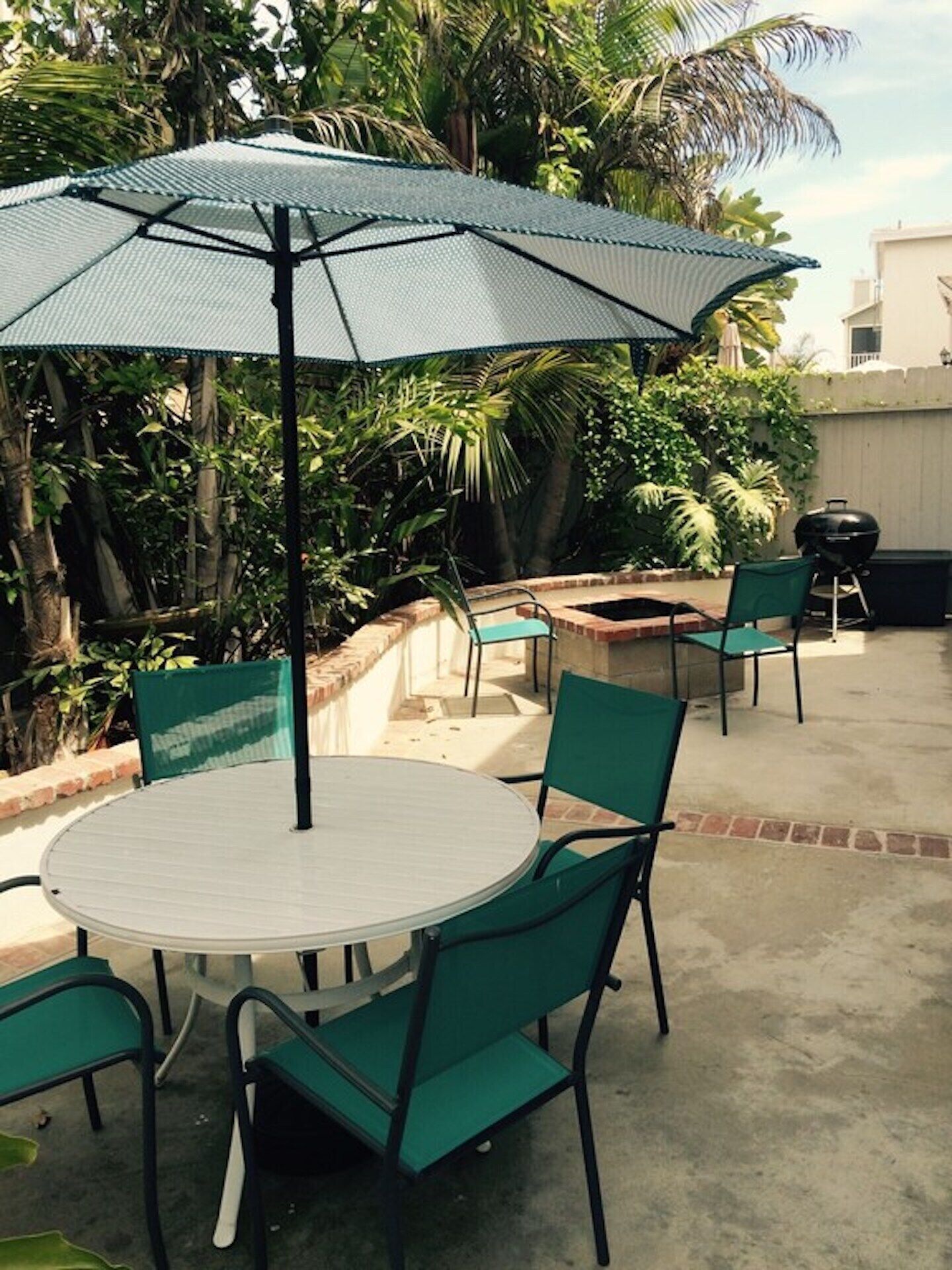 Un patio con una mesa redonda y sillas, una sombrilla grande y una parrilla.