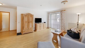 A living room with a television, wooden cabinets, a sofa, and a table. - Apartment 'Fewo Brünnstein- Nr 28 Pool, Sauna' with Mountain View, Shared Garden & Wi-Fi (Oberaudorf)