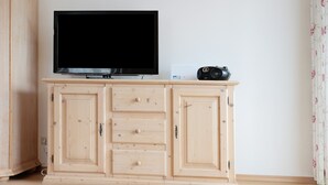 A room with a television on a wooden cabinet, a speaker, and a floral curtain. - Apartment 'Fewo Brünnstein- Nr 28 Pool, Sauna' with Mountain View, Shared Garden & Wi-Fi (Oberaudorf)