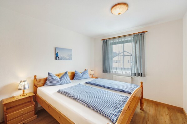 Un lit double avec une literie à carreaux, une table de chevet avec une lampe, une fenêtre avec des rideaux et un tableau au mur.